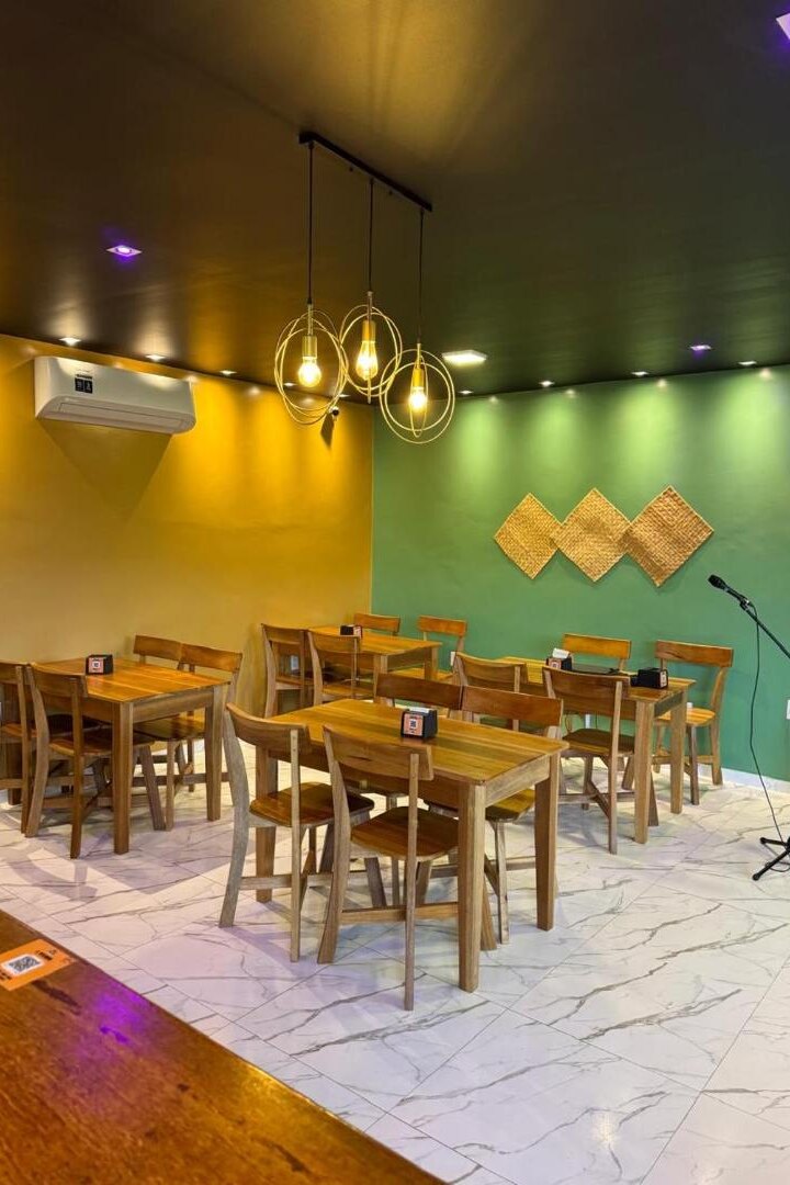 Salão de refeições com mesas de madeira e luminárias pendentes